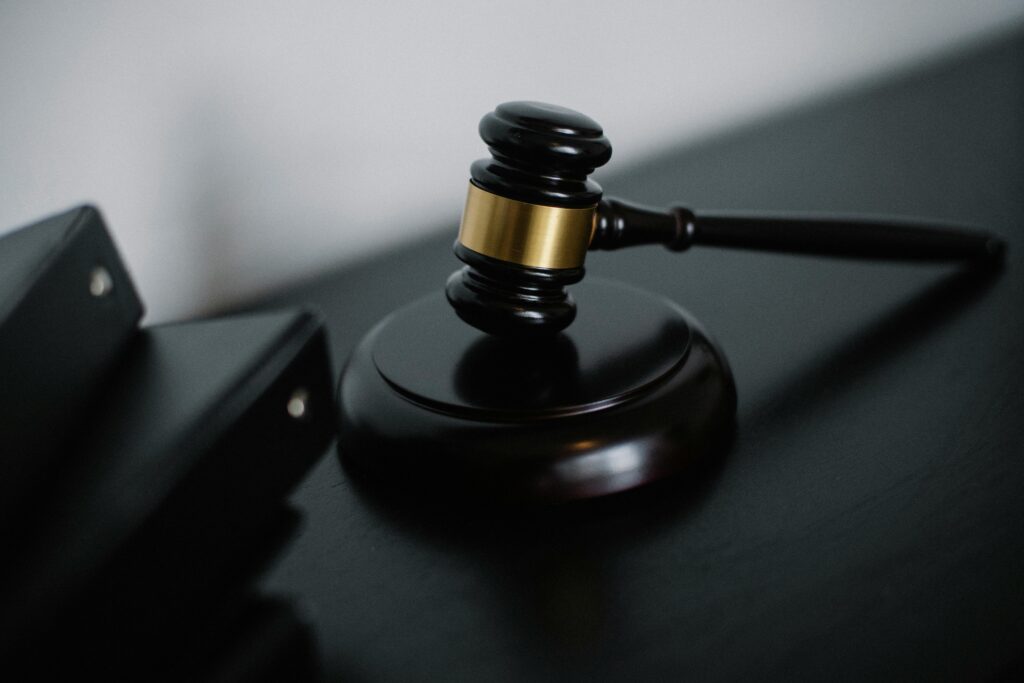 A close-up of a judge's gavel resting on a sound block beside black legal binders on a dark surface.